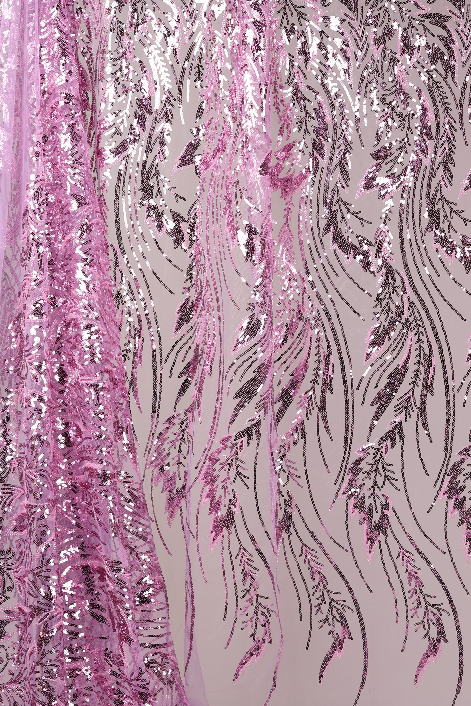 a close-up view of a fabric with a floral pattern in shades of pink and purple. The fabric appears to be sequined, with a repeating pattern of pink and purple lines and leaves. The fabric is hanging, creating a visually striking and intricate design.
