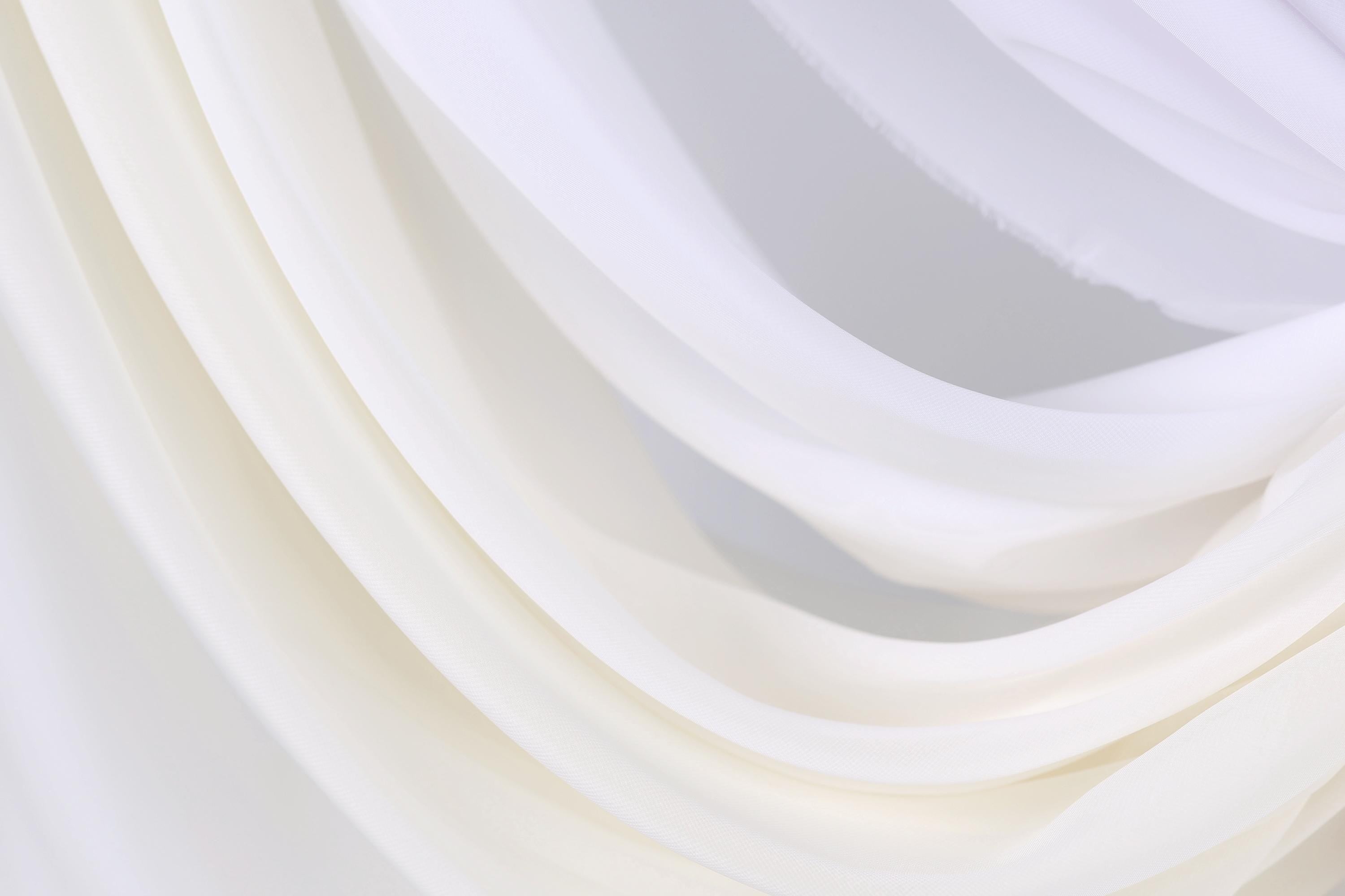 The image is a close-up of a white fabric, possibly a sheer or sheer-like material, with a soft, flowing texture.