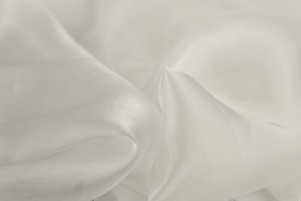 The image is a close-up of a soft, white fabric, possibly silk or chiffon, with a slightly wrinkled texture.