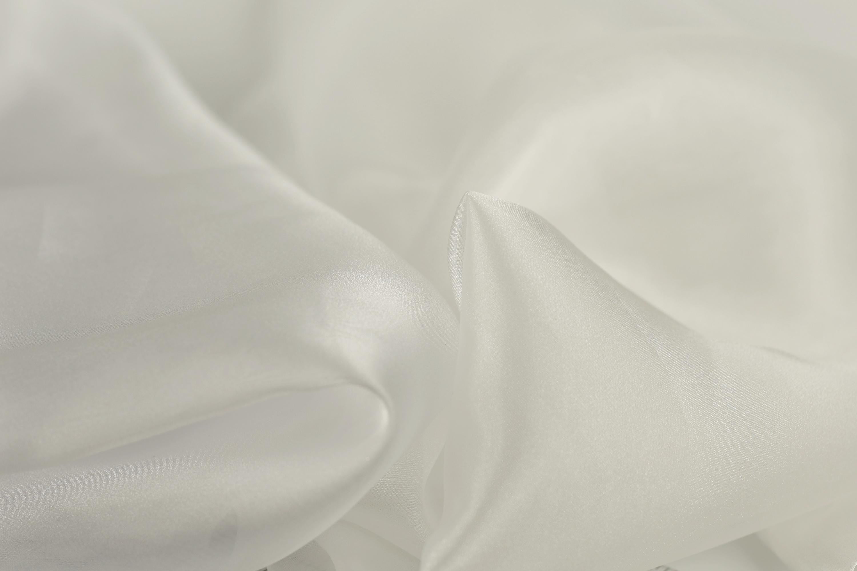 The image is a close-up of a soft, white fabric, possibly silk or chiffon, with a slightly wrinkled texture.