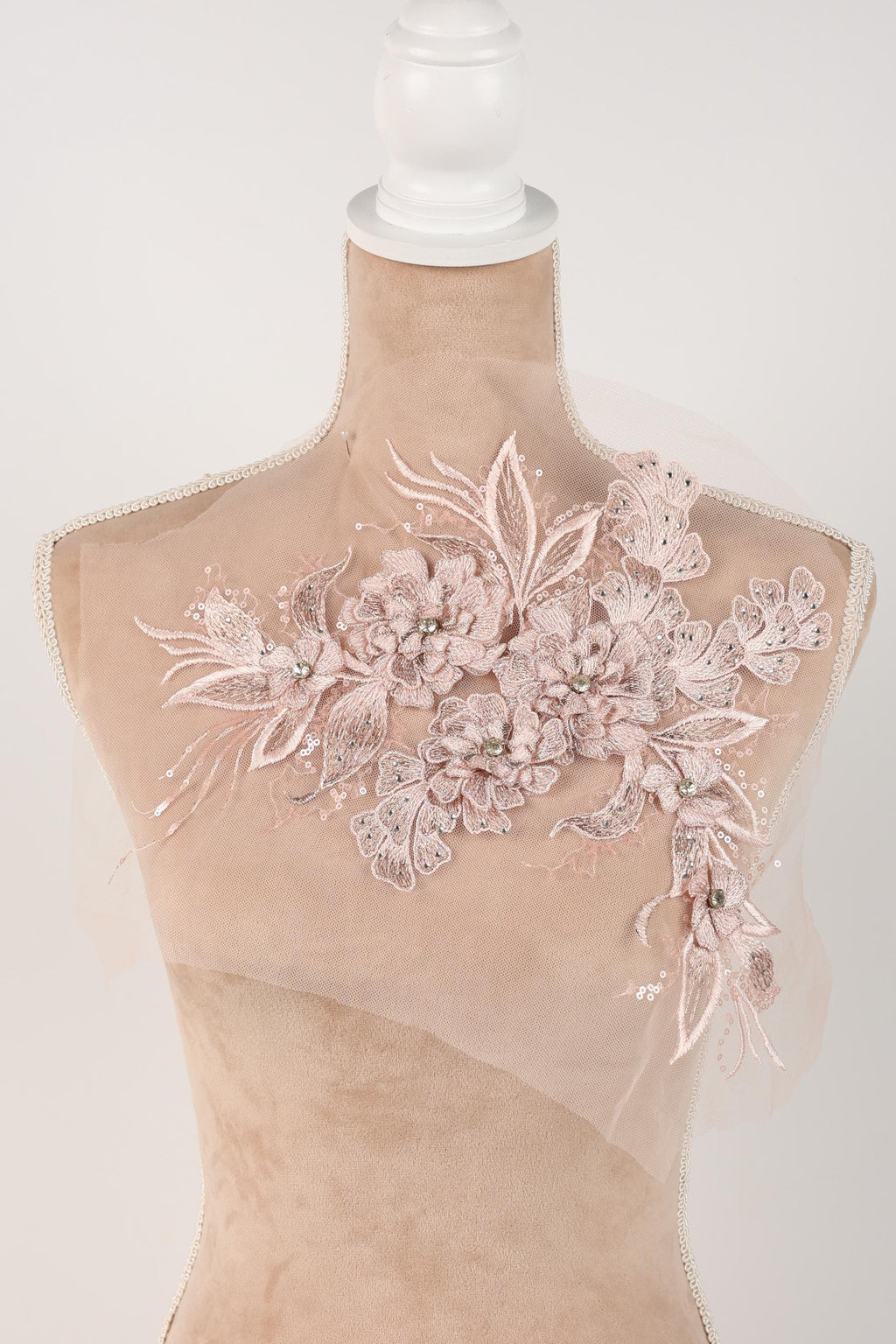 A close-up view of a delicate, beige-colored fabric with intricate floral embroidery.