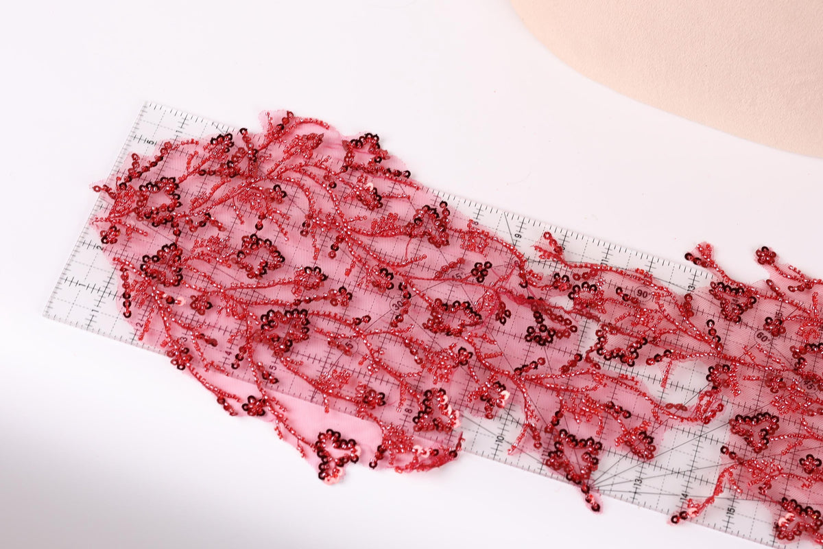 a close-up view of a piece of fabric with a floral pattern, featuring red sequins or beads that appear to be attached to the fabric.