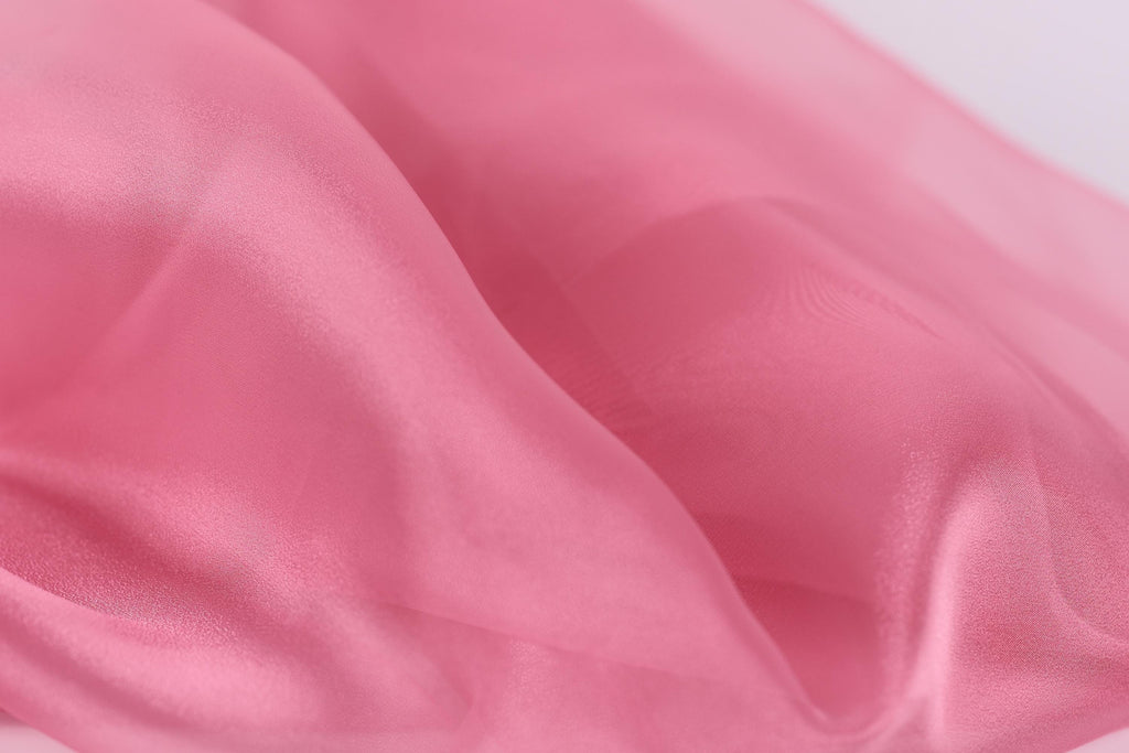 A close-up view of a soft, flowing pink fabric, possibly silk or chiffon, with a smooth and shiny texture.