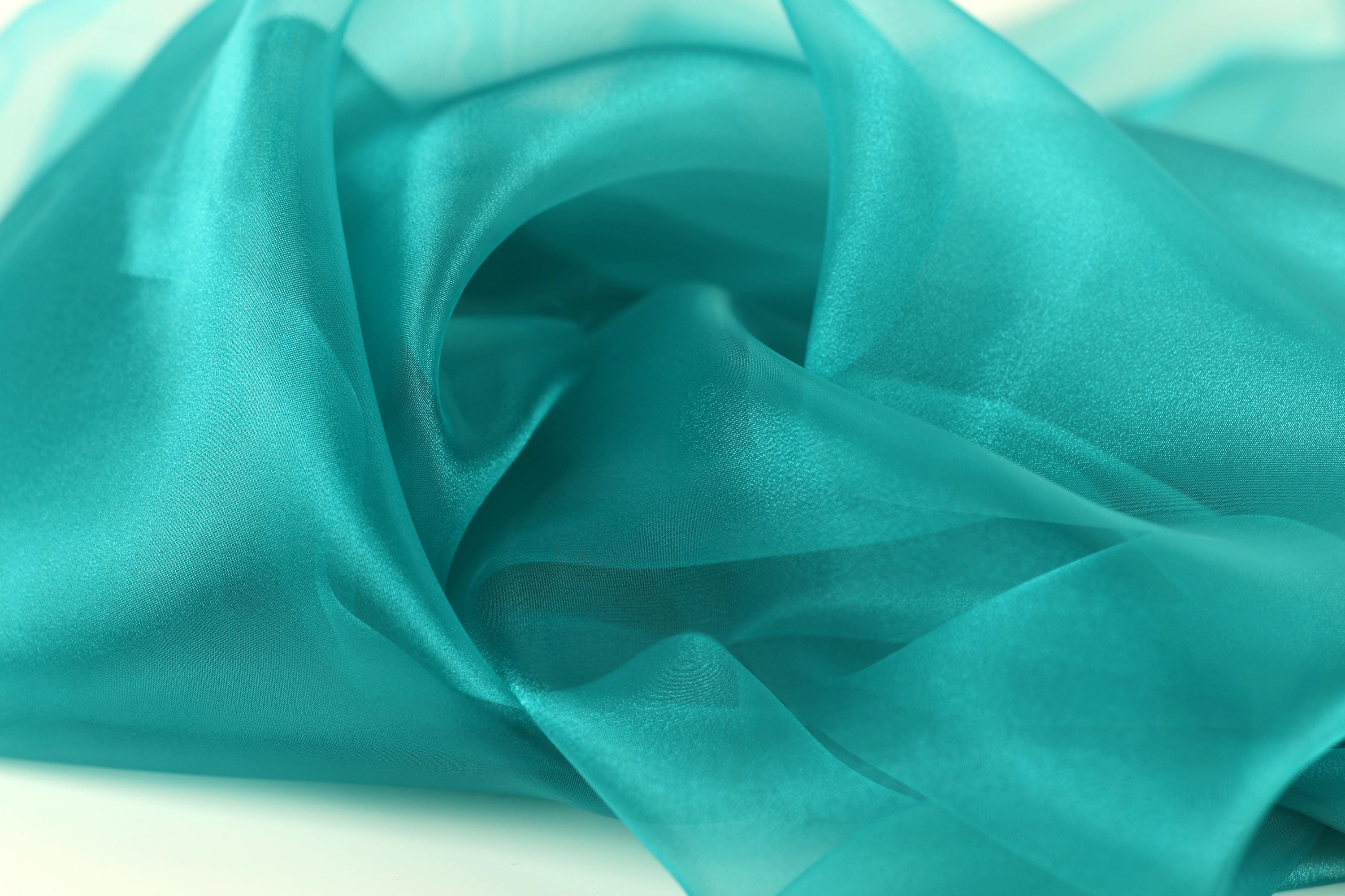 The image is a close-up of a fabric with a turquoise color, appearing soft and flowing.