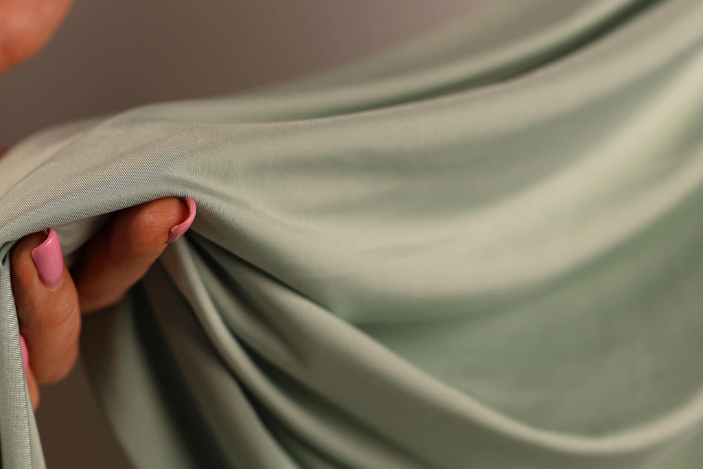 A hand holding a piece of green fabric, with the fingers visible and the fabric partially draped over the hand.