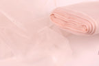 A close-up view of a soft, light pink fabric, possibly tulle, with a rolled-up end visible.