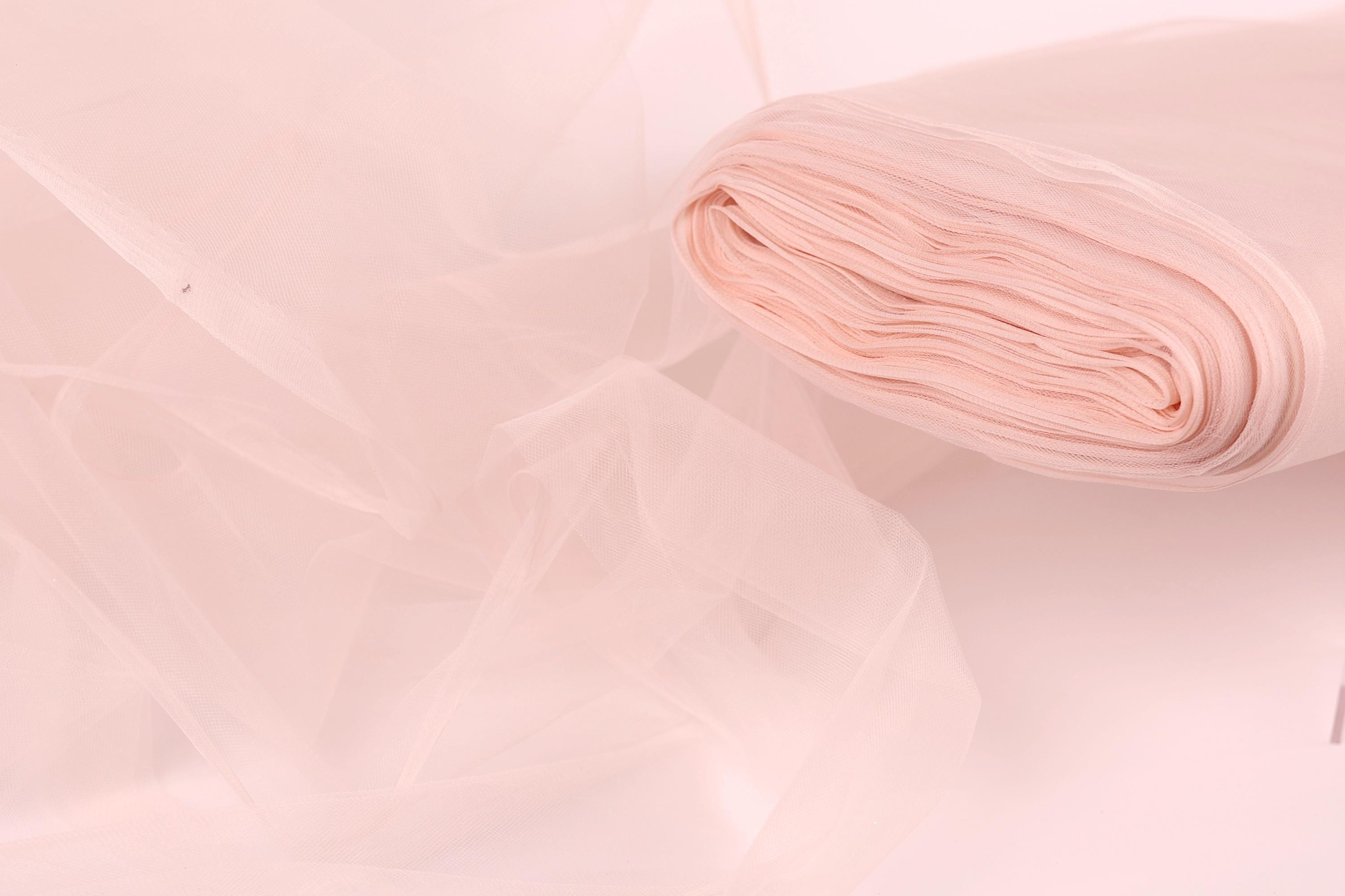A close-up view of a soft, light pink fabric, possibly tulle, with a rolled-up end visible.