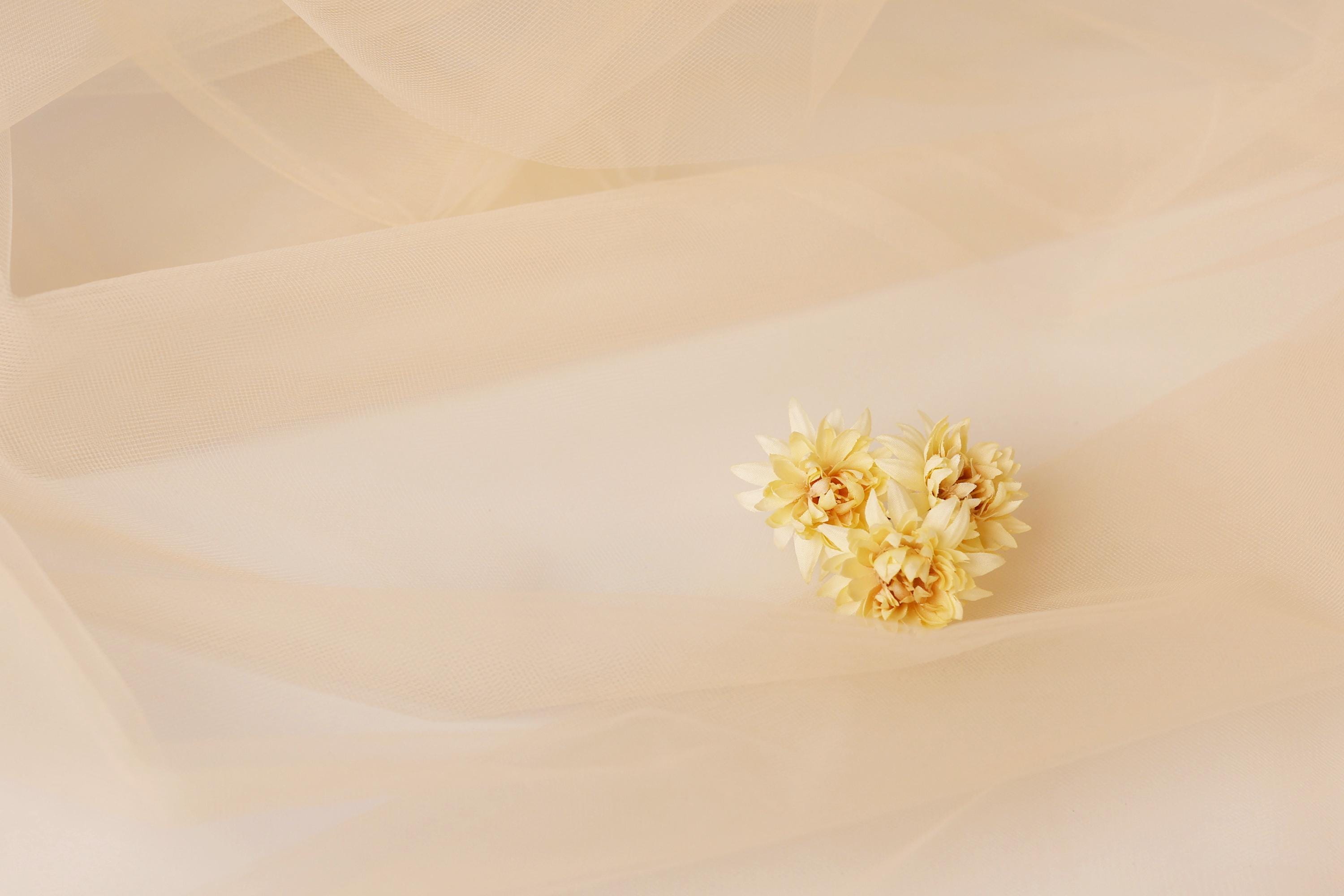 A single yellow flower is resting on a light beige fabric, creating a simple and elegant composition.