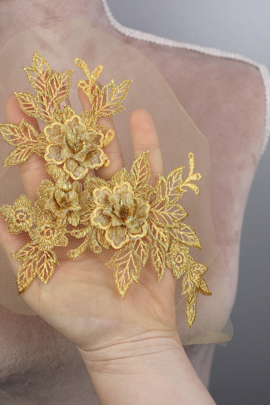 A hand holding a delicate gold floral embroidered piece of fabric.