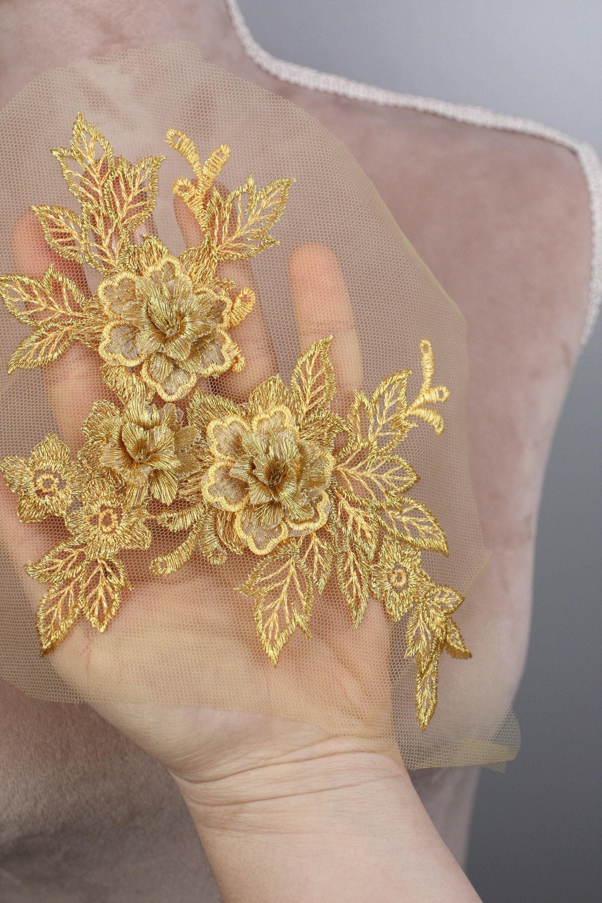 A hand holding a delicate gold floral embroidered piece of fabric.