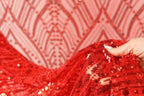 A hand is holding a piece of red sequin fabric, with the fabric's intricate patterns and textures visible.
