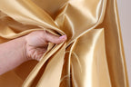 A hand is holding a piece of gold fabric, which appears to be a shiny, shiny material.
