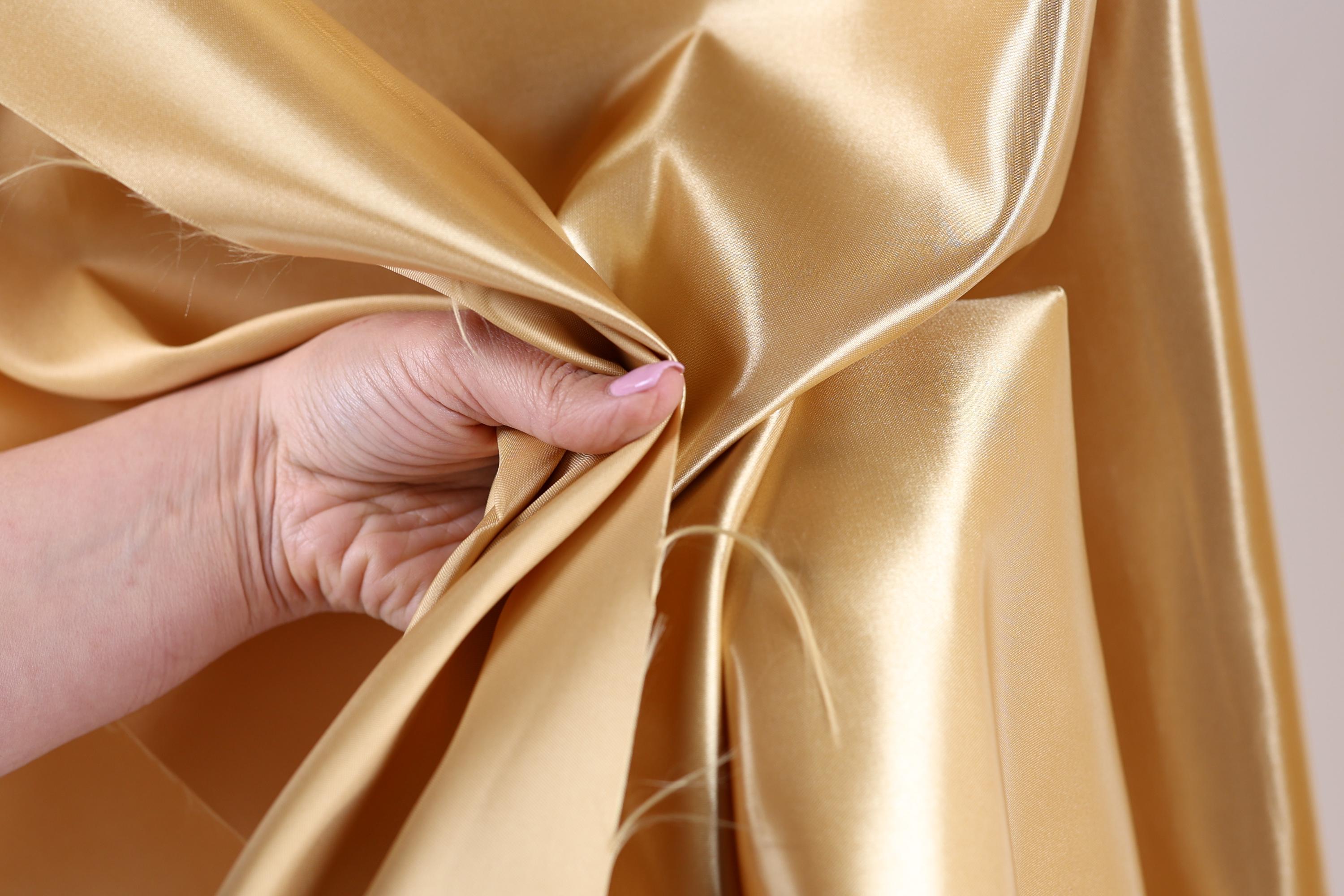 A hand is holding a piece of gold fabric, which appears to be a shiny, shiny material.