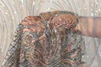 A close-up view of a hand holding a piece of sequined fabric, with the fabric's intricate patterns and shimmering beads visible.