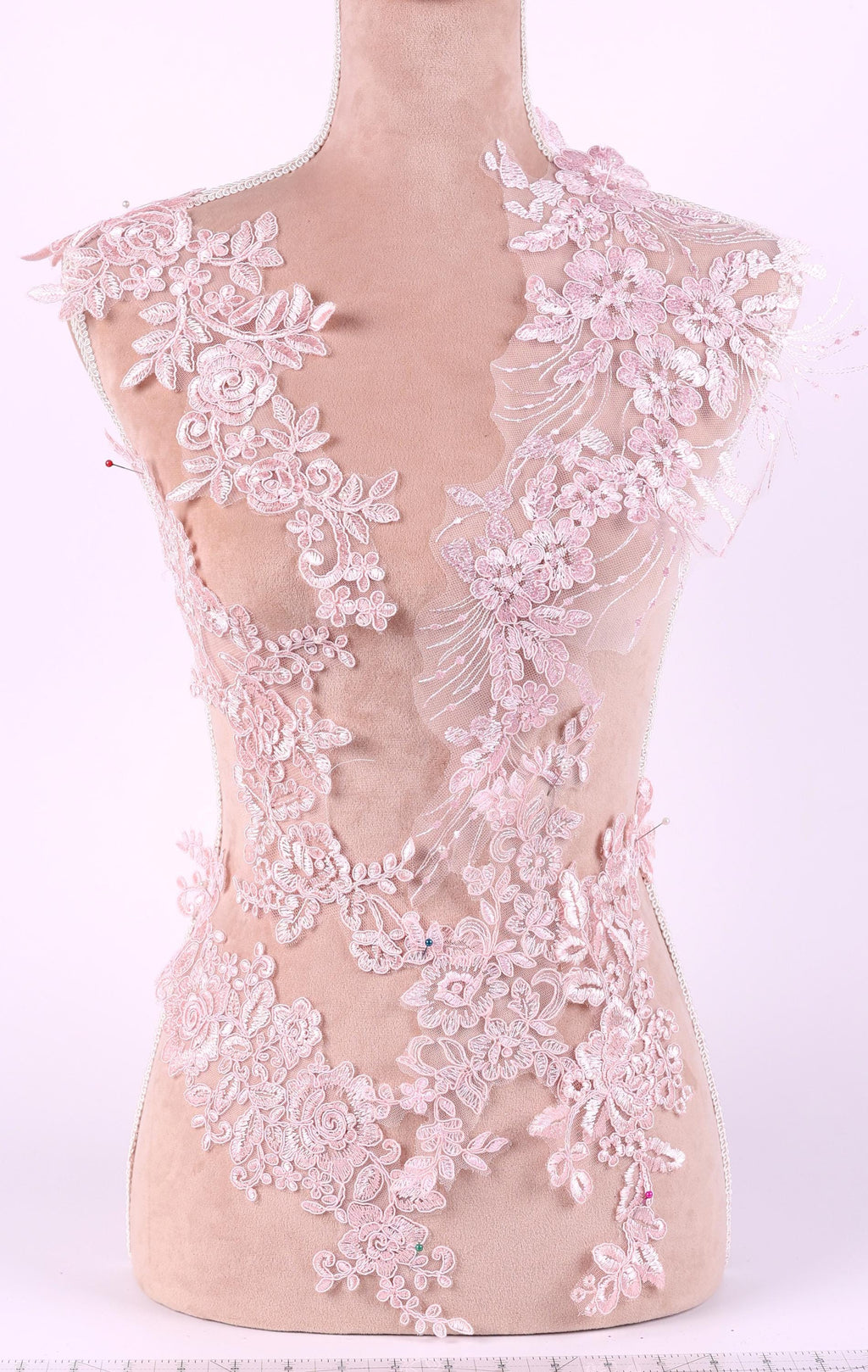A mannequin is wearing a dress with intricate pink lace details, including floral and leaf patterns.