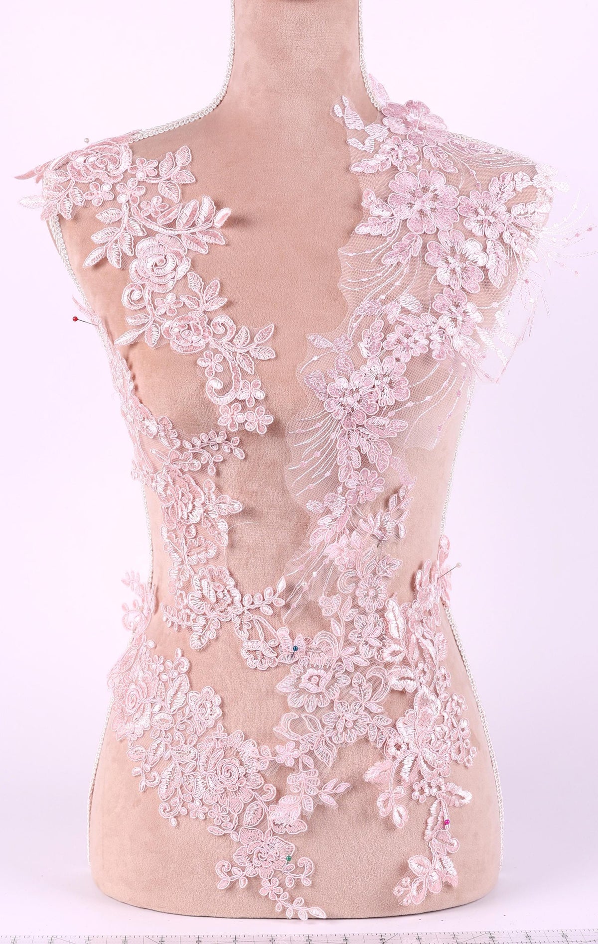 A mannequin is wearing a dress with intricate pink lace details, including floral and leaf patterns.