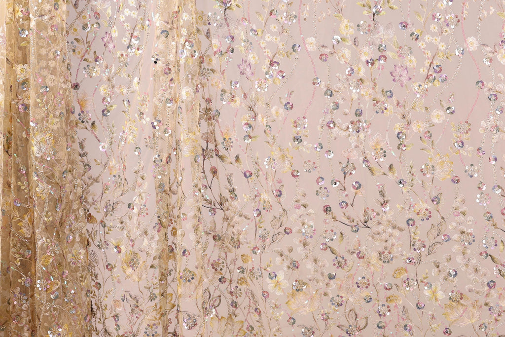 a close-up view of a delicate, intricately embroidered fabric with a floral pattern. The fabric appears to be made of sheer material, with a blend of gold and pink colors. The pattern is composed of numerous small flowers and leaves, creating a visually appealing and detailed design. The fabric is spread across the entire frame, showcasing its intricate design and the craftsmanship involved in its creation.