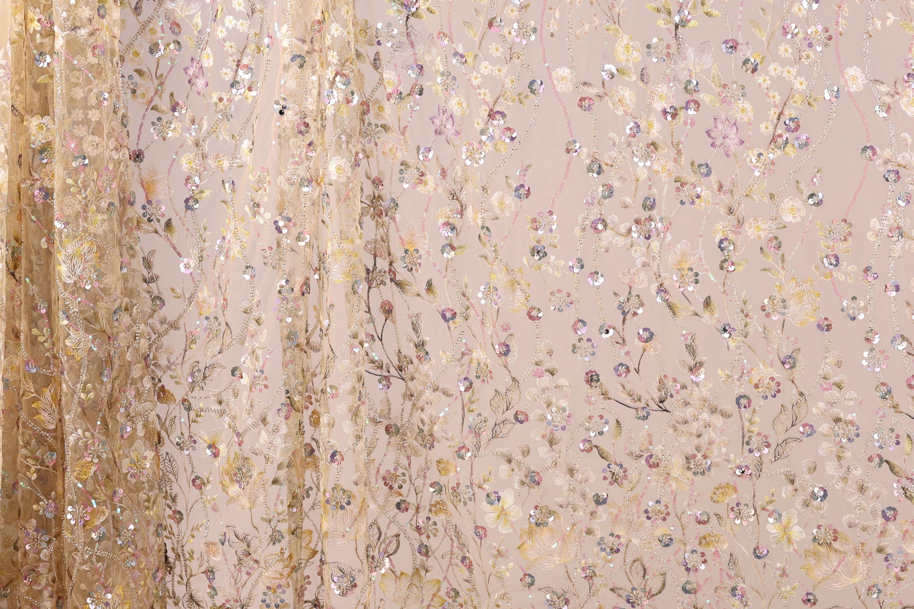 a close-up view of a delicate, intricately embroidered fabric with a floral pattern. The fabric appears to be made of sheer material, with a blend of gold and pink colors. The pattern is composed of numerous small flowers and leaves, creating a visually appealing and detailed design. The fabric is spread across the entire frame, showcasing its intricate design and the craftsmanship involved in its creation.