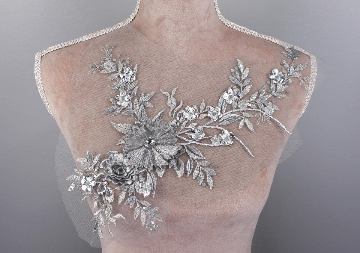 A mannequin torso with a delicate, intricate silver floral embroidery on the bust area.
