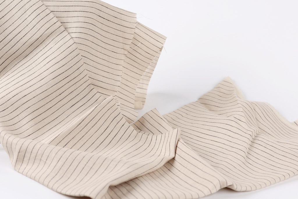 a close-up view of a fabric with a striped pattern, featuring a mix of horizontal and vertical stripes in varying shades of beige.