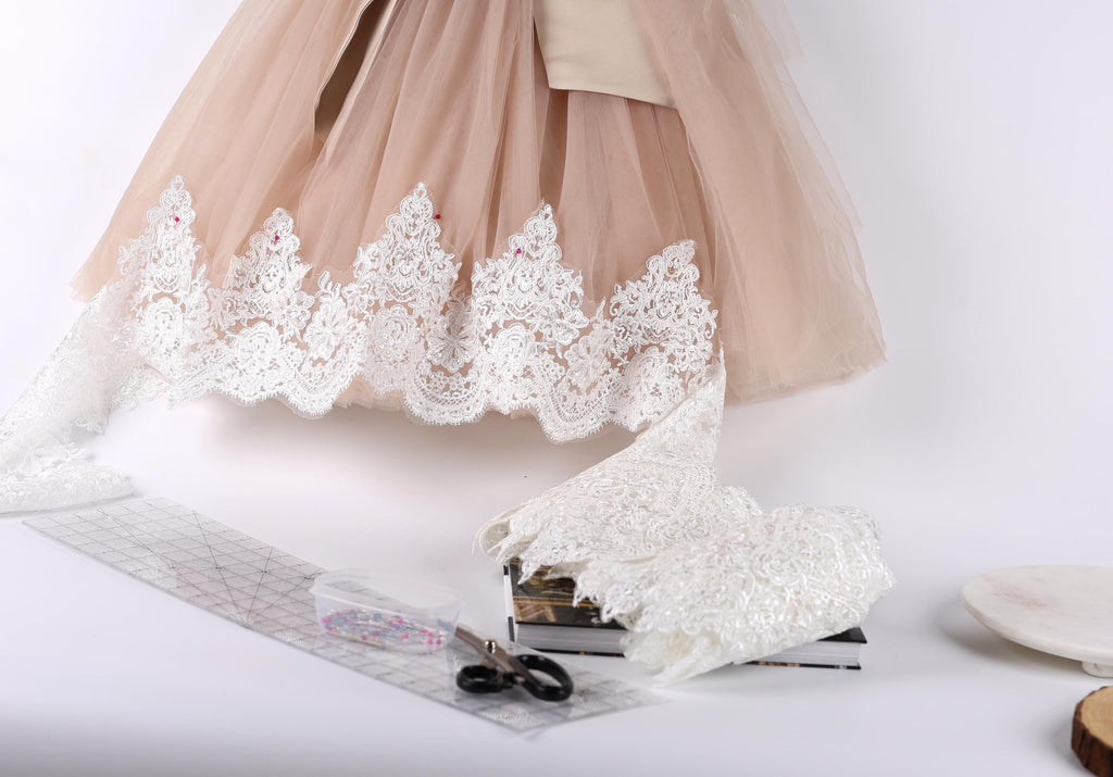 a light pink tulle skirt with white lace trim, along with a pair of scissors, a ruler, and some books.