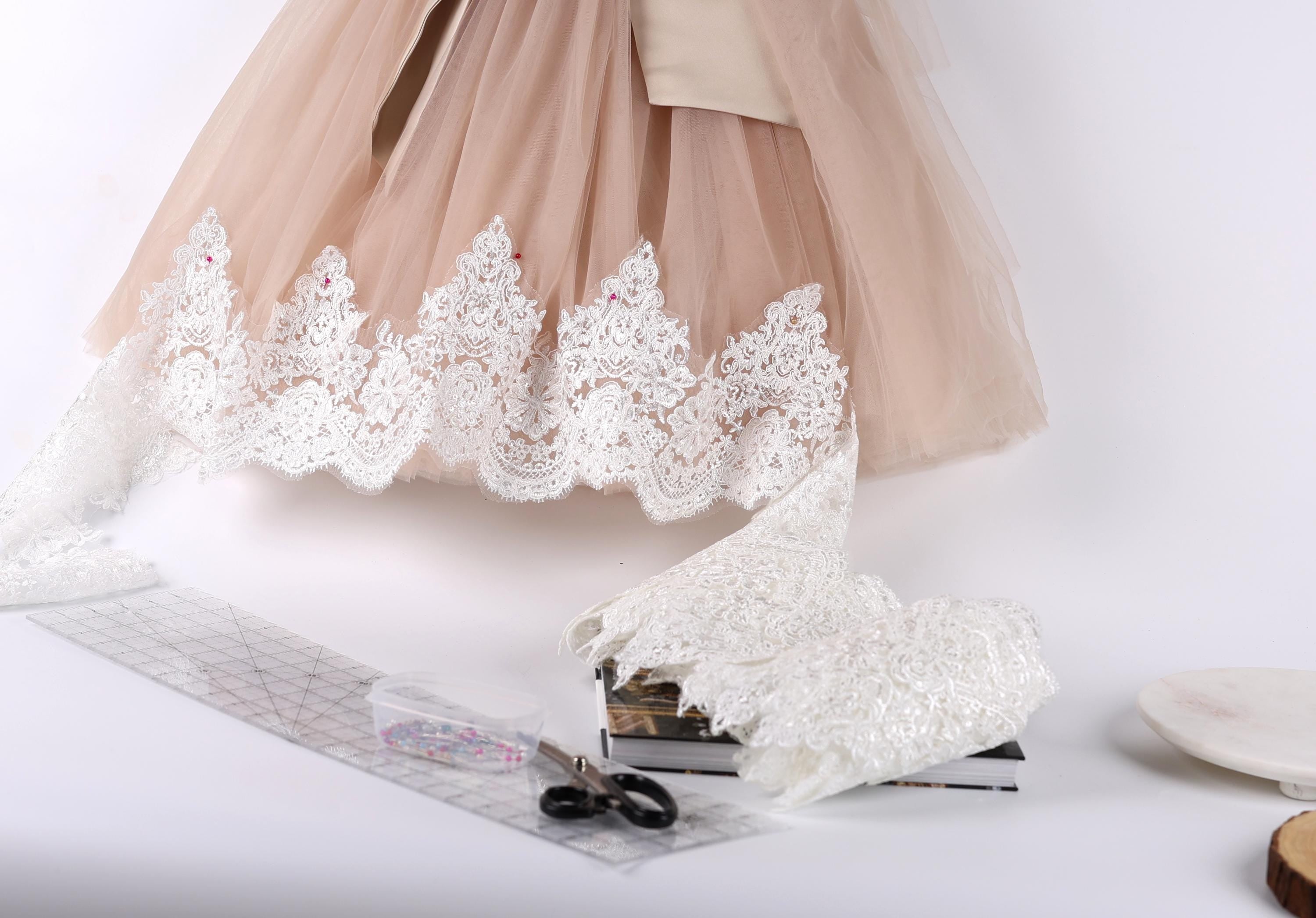 a light pink tulle skirt with white lace trim, along with a pair of scissors, a ruler, and some books.