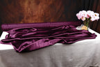 a table with a purple satin fabric draped over it, and a vase of pink flowers placed next to it.