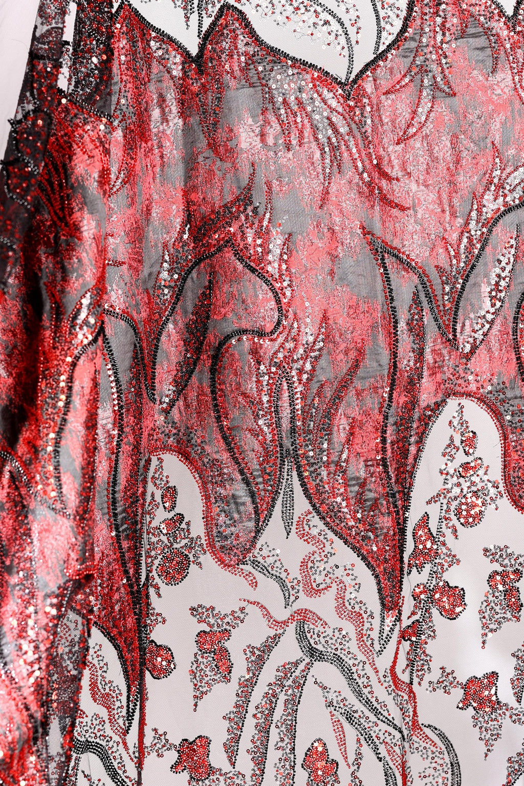 a close-up view of a fabric with a striking red and black pattern, including floral and leaf-like designs. The fabric appears to be made of a shiny, sequined material, adding a touch of sparkle and elegance to the overall appearance.
