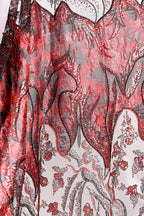 a close-up view of a fabric with a striking red and black pattern, including floral and leaf-like designs. The fabric appears to be made of a shiny, sequined material, adding a touch of sparkle and elegance to the overall appearance.