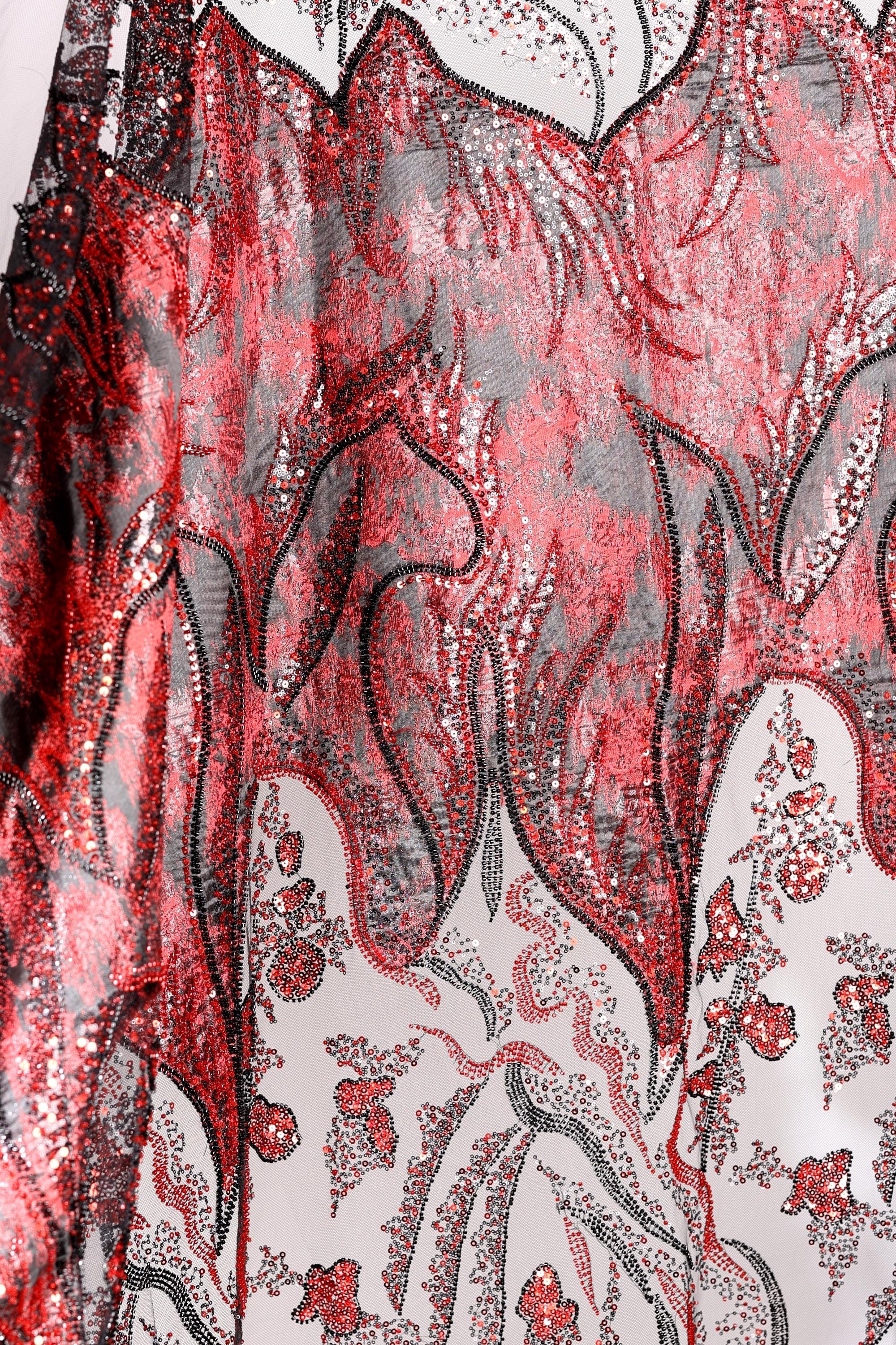 a close-up view of a fabric with a striking red and black pattern, including floral and leaf-like designs. The fabric appears to be made of a shiny, sequined material, adding a touch of sparkle and elegance to the overall appearance.