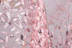 a close-up view of a delicate, pink, and white lace fabric with a floral pattern. The fabric appears to be made of sheer material, giving it a delicate and airy appearance. The lace is intricately embroidered with small sequins, adding a touch of sparkle and elegance to the design. The background of the image is a light pink color, which complements the pink and white of the lace fabric.