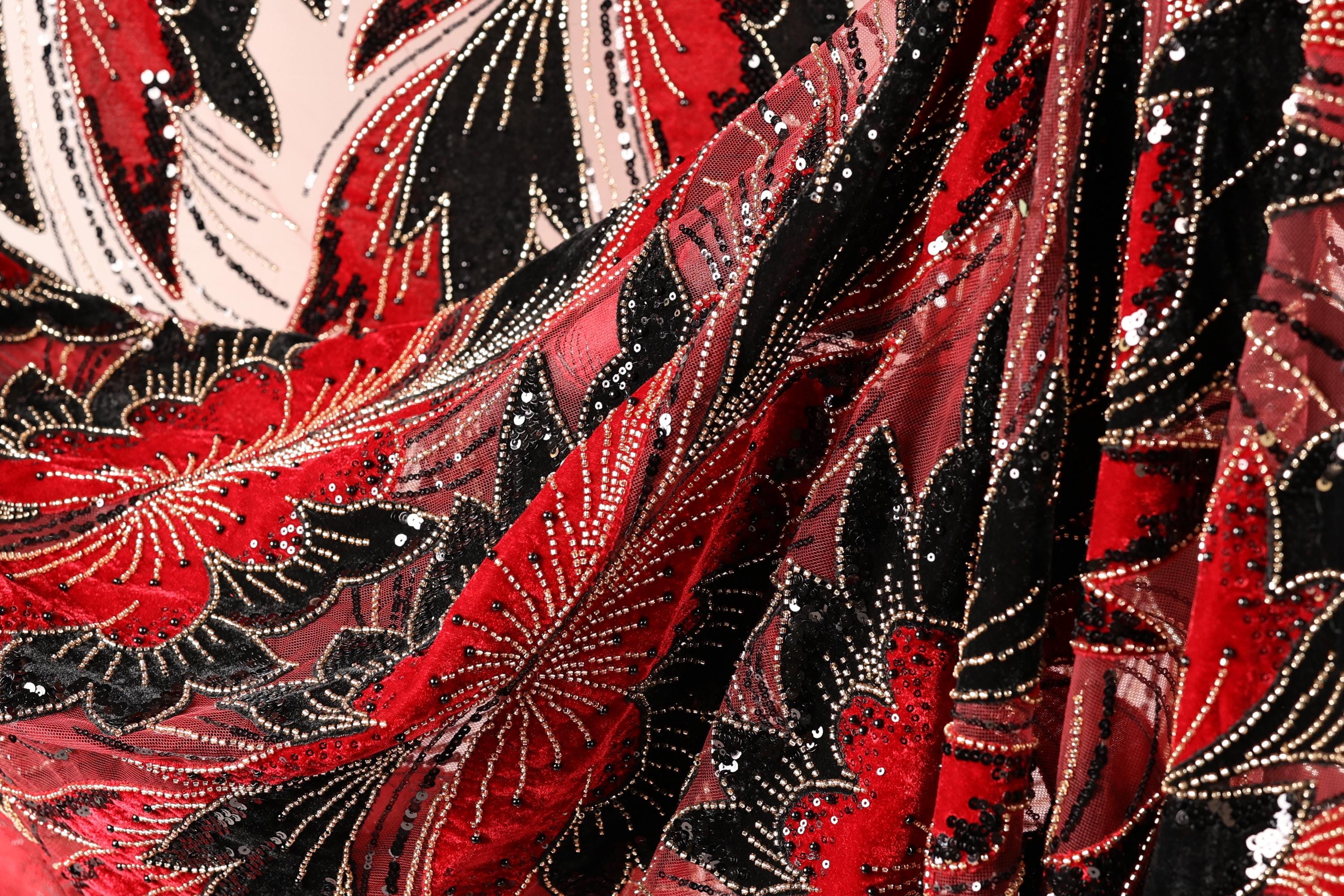 The image is a close-up of a fabric with a floral pattern in red, black, and white. The fabric appears to be made of sequin material, with a shiny, glittery appearance.