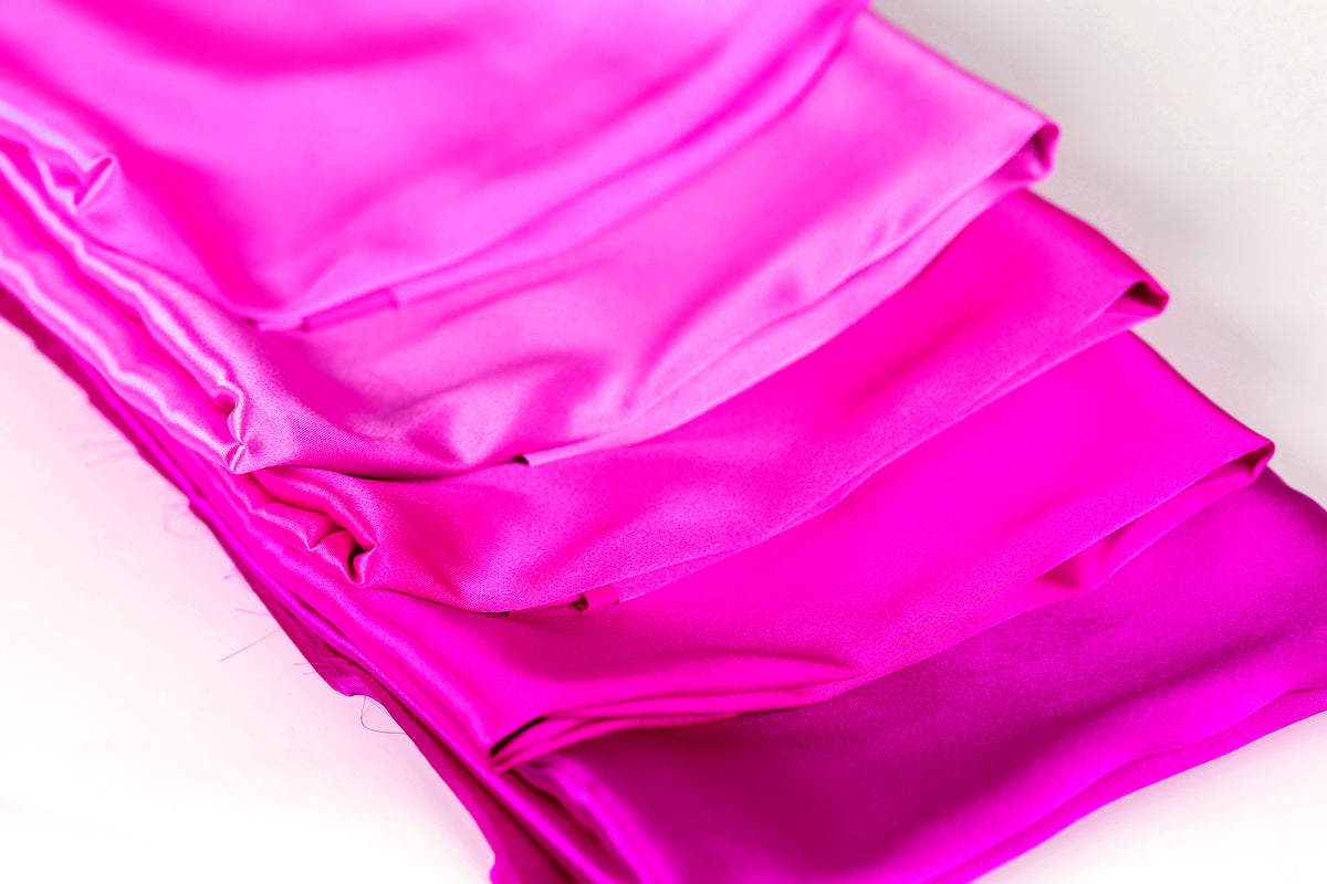 A close-up image of a pile of shiny, vibrant pink fabric.