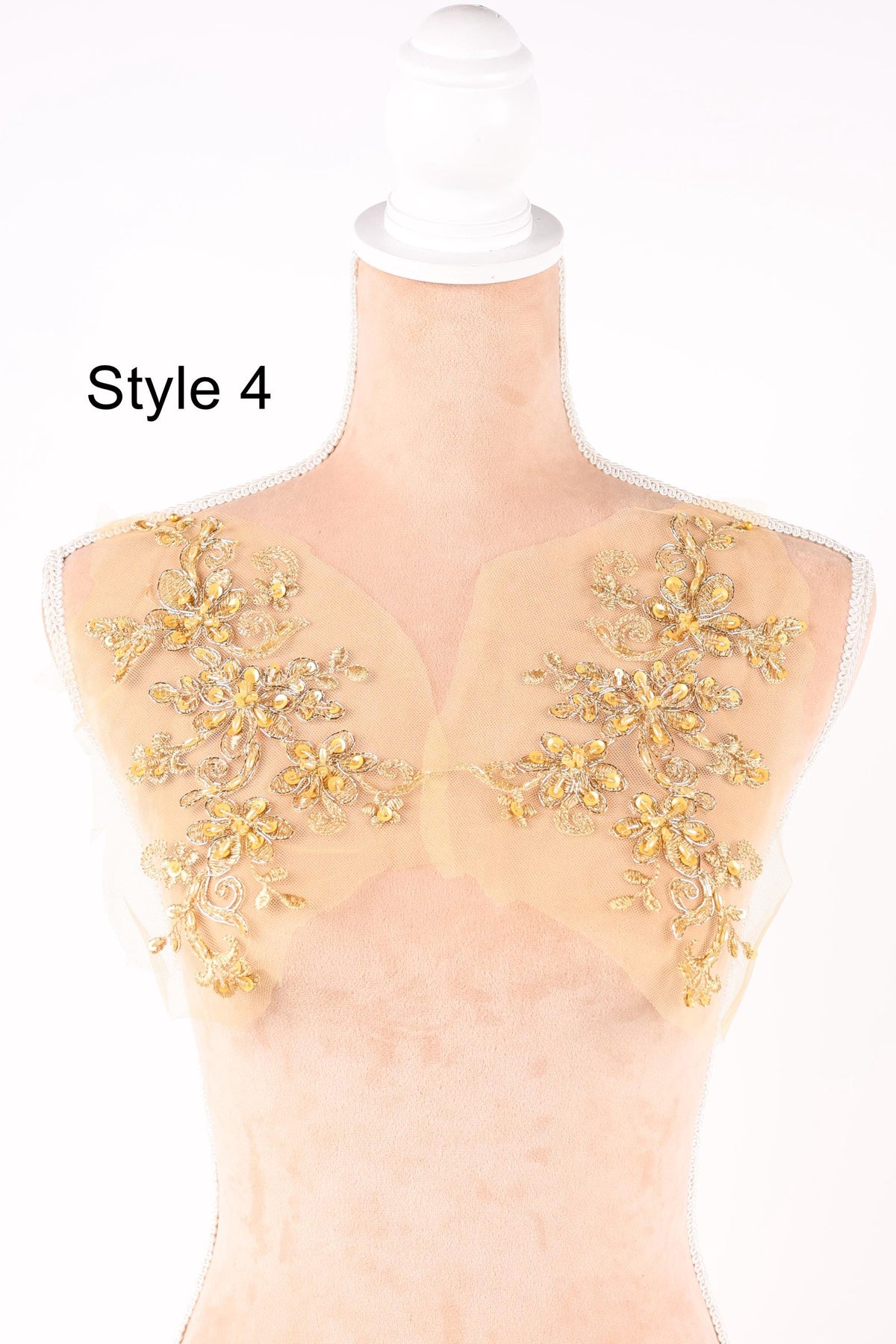 A mannequin with a beige dress and gold floral embroidery on the shoulders.