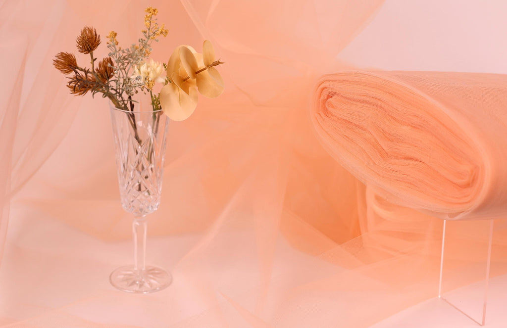 a clear glass vase filled with flowers, placed on a table against a peach-colored background.