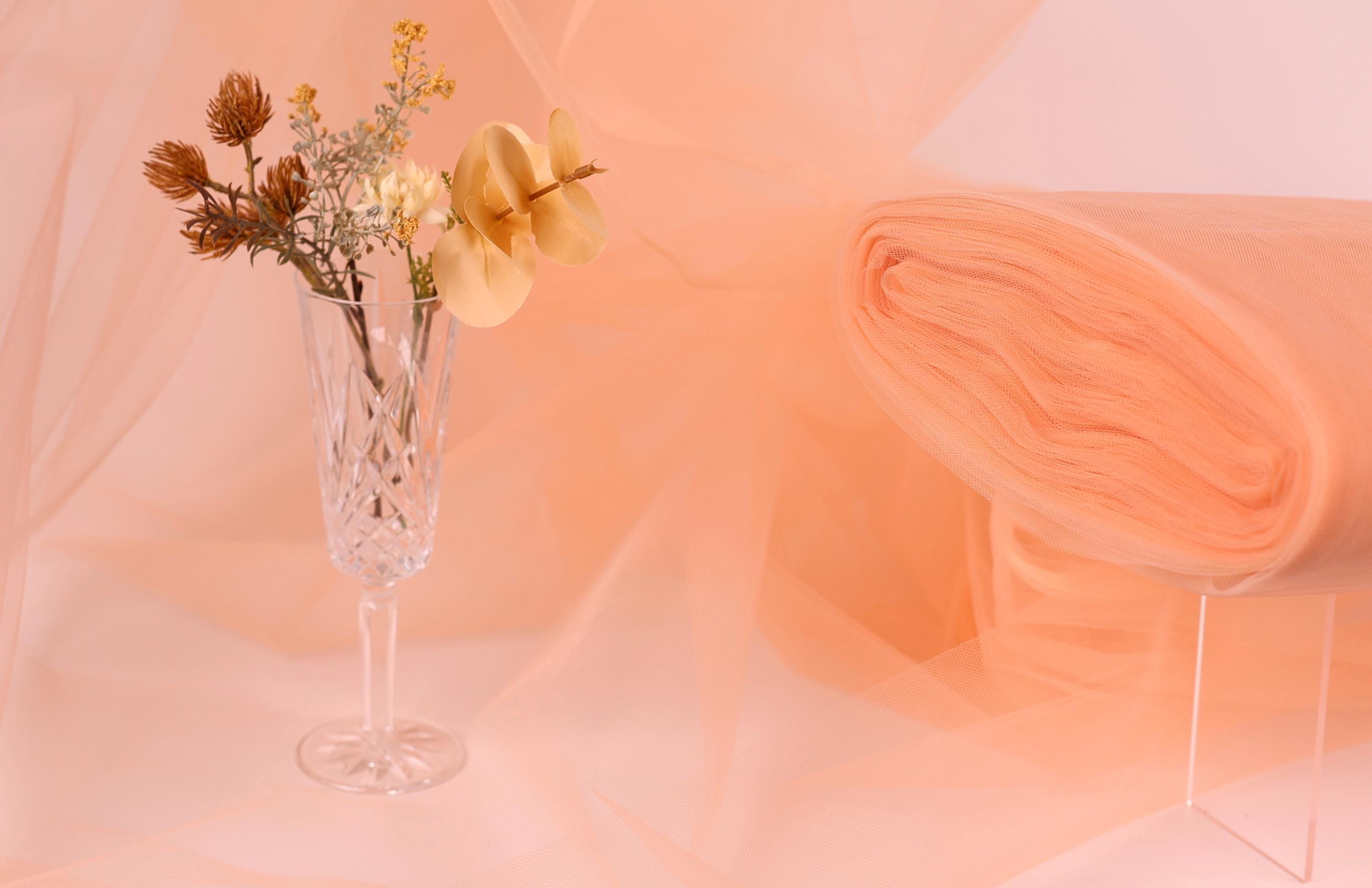 a clear glass vase filled with flowers, placed on a table against a peach-colored background.