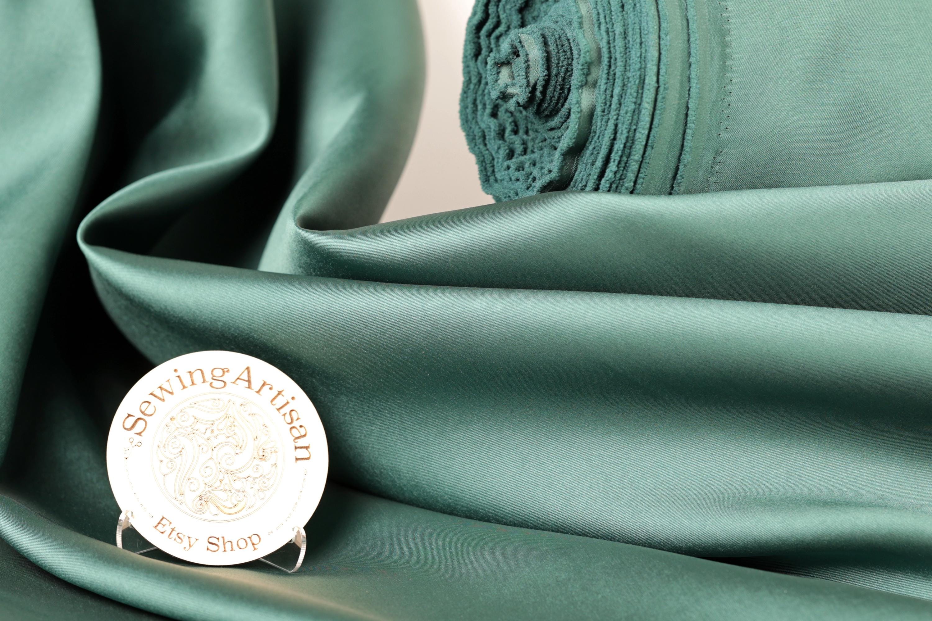 a close-up of a green satin fabric, with a white circular sign displaying the text "Sewing Artist Ety Shop" placed on it.