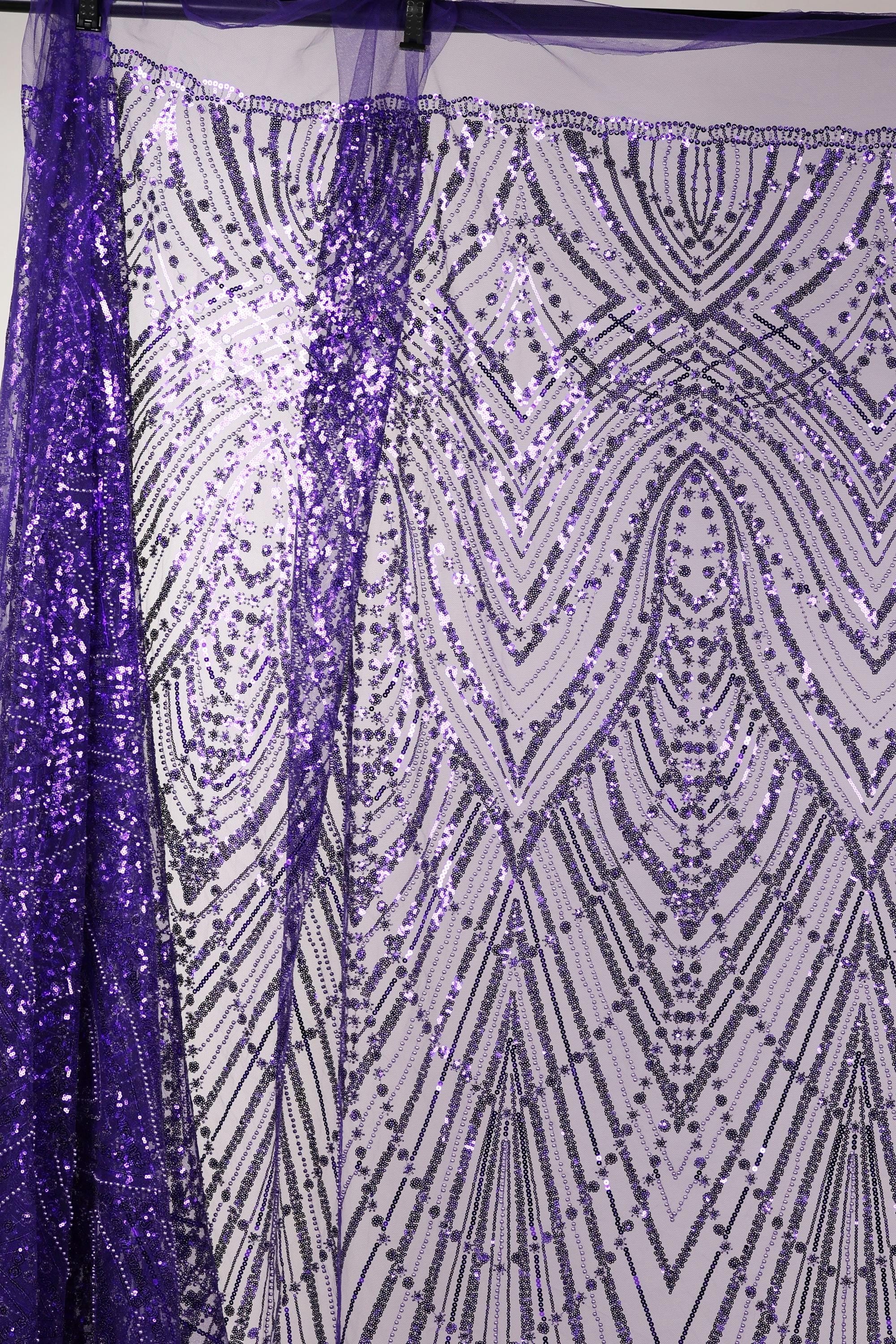 a close-up view of a sequin fabric with a purple and white pattern. The fabric appears to be made of a shiny, metallic material and has a repeating pattern of lines and dots in shades of purple and white. The fabric is hanging on a rod, and the background is a plain white wall.