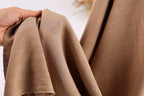 A hand is holding a piece of brown fabric, which appears to be a soft, textured material.