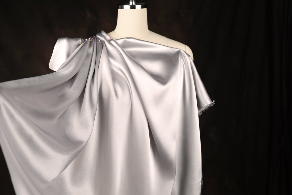 A mannequin wearing a gray satin dress with a draped, flowing design.