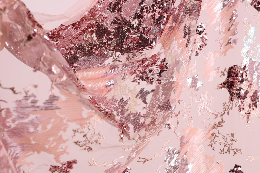 The image is a close-up of a fabric with a pink and red floral pattern, featuring sequins and lace-like textures.
