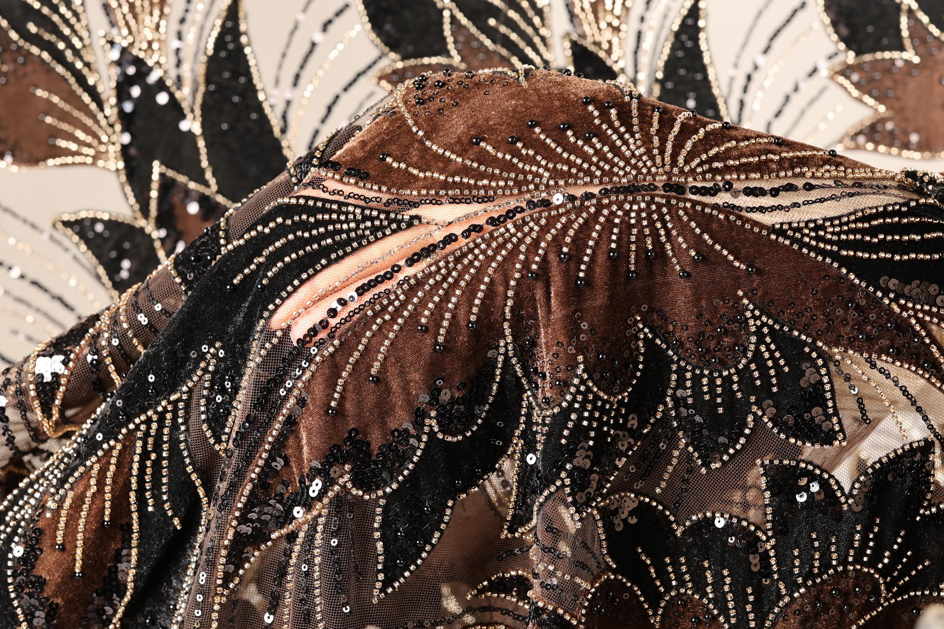 The image is a close-up of a fabric with a floral pattern, featuring a mix of brown, black, and gold colors. The fabric appears to be made of sequin material, with a detailed and intricate design.