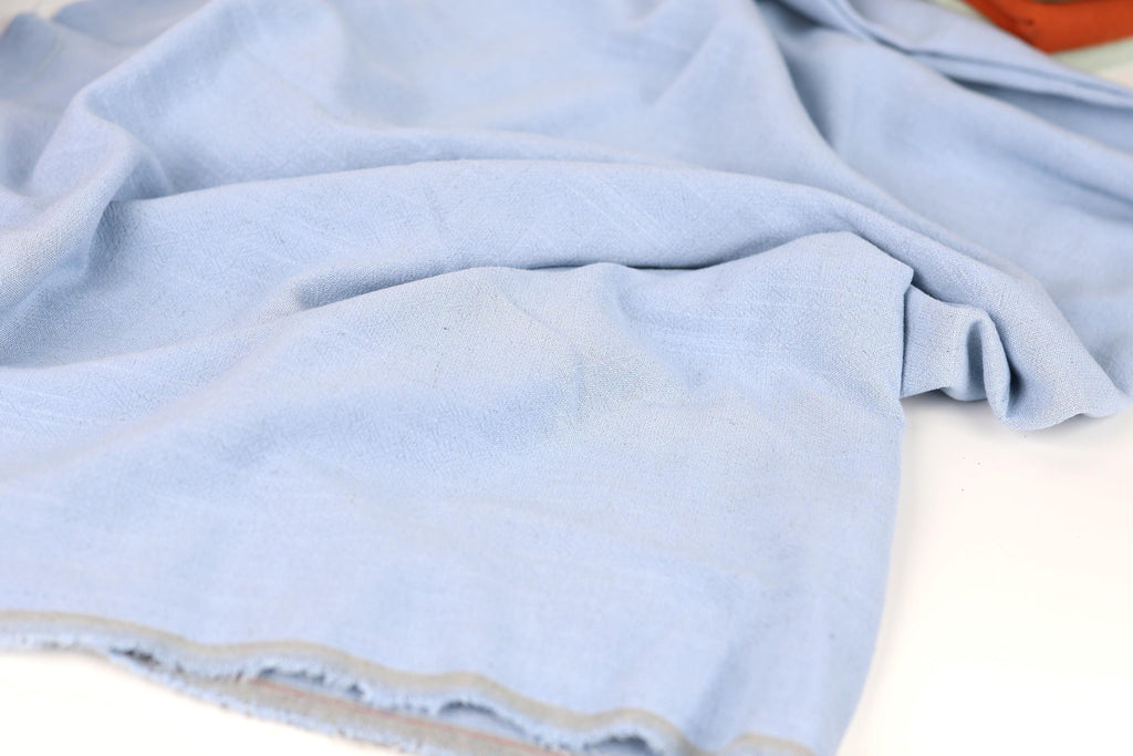 A close-up view of a light blue fabric, possibly a piece of clothing or a textile, with a slightly wrinkled and crumpled appearance.