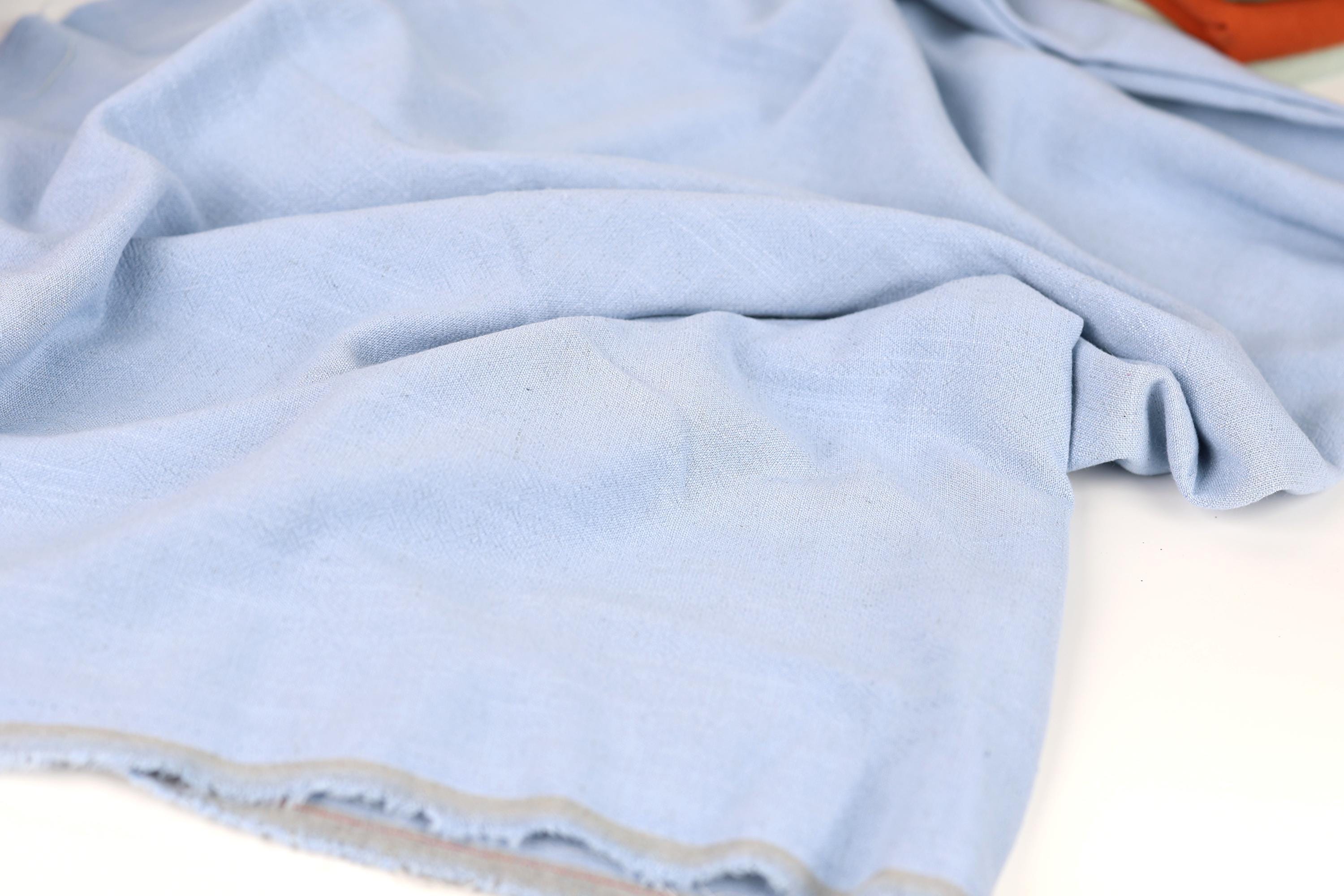 A close-up view of a light blue fabric, possibly a piece of clothing or a textile, with a slightly wrinkled and crumpled appearance.