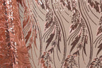 a close-up view of a fabric with a repeating pattern of pink and brown sequin designs. The pattern appears to be a floral or leaf-like design, with the sequins creating a textured and intricate appearance.