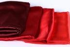 a close-up view of a pile of red and burgundy satin fabric, with the fabric appearing to be folded or rolled up.