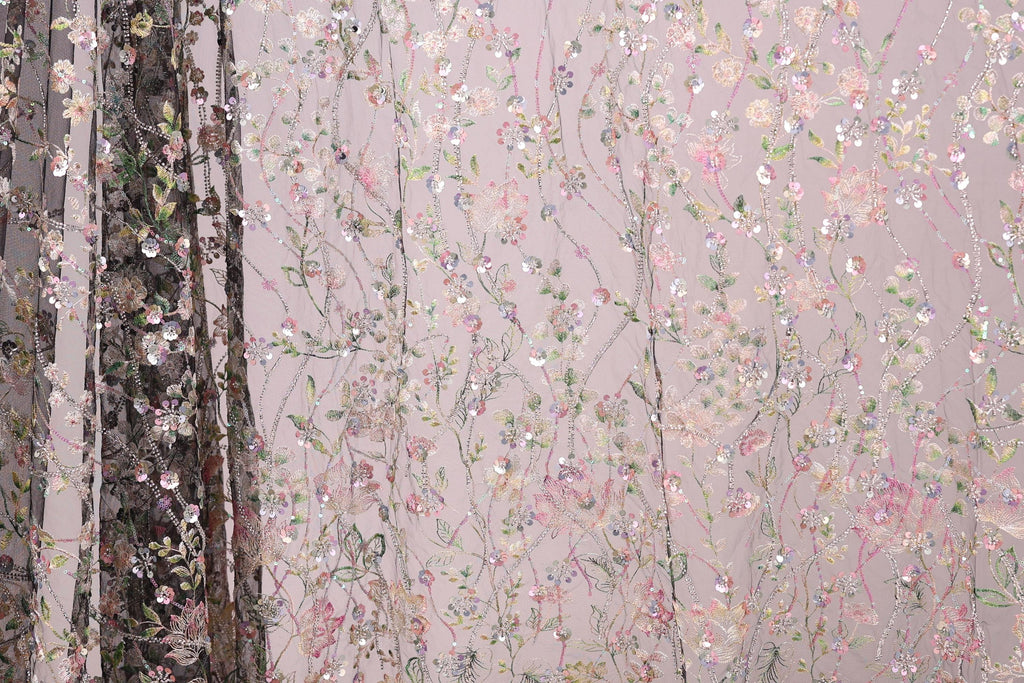 a close-up view of a fabric with a floral pattern, including pink and green flowers, as well as leaves and branches. The fabric appears to be made of a sheer material, giving it a delicate and airy appearance. The background of the image is a light pink color, which complements the floral pattern on the fabric.