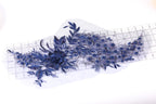 a close-up view of a piece of fabric with a floral pattern, including blue flowers and leaves. The fabric appears to be a lace or embroidered material, with a ruler visible in the background.