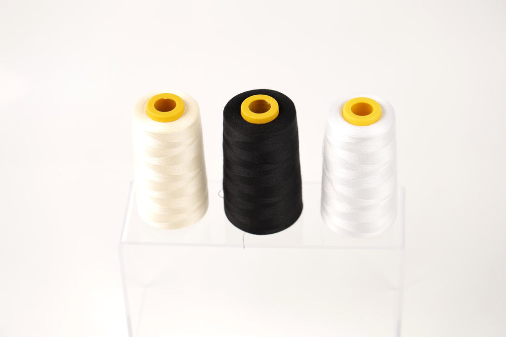 Three spools of thread in white, black, and white are displayed on a clear stand against a white background.