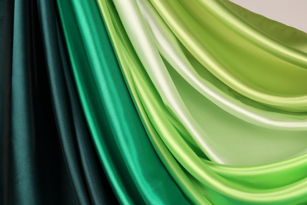 a close-up view of a collection of colorful satin fabric, with a gradient of green and black hues. The fabric appears to be folded or draped, creating a visually striking and textured composition.